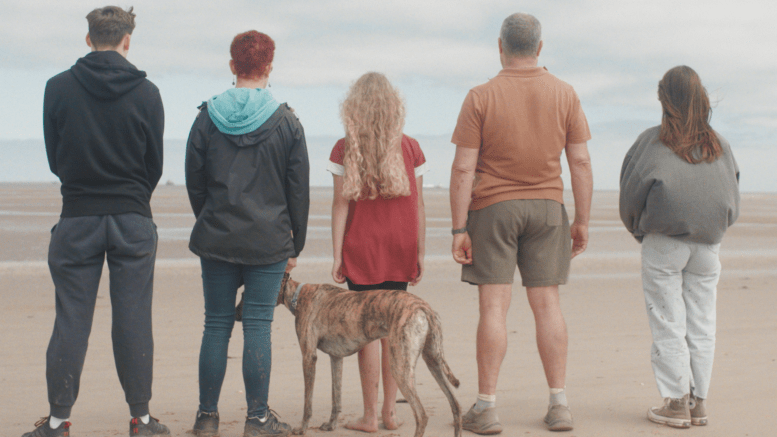 Five people and a dog stood o a beach looking away